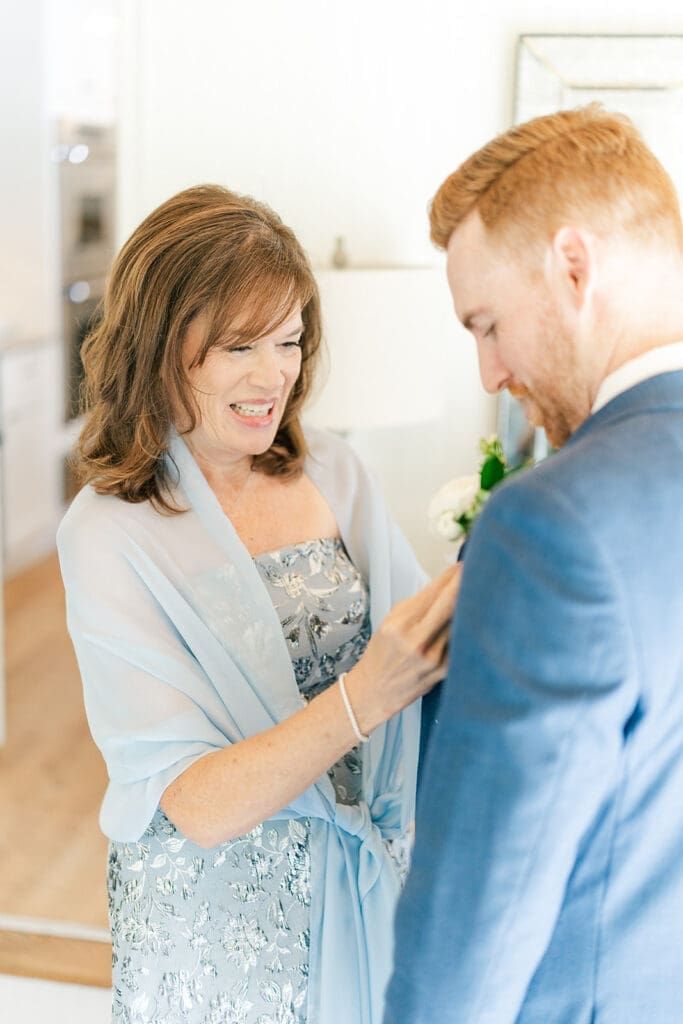 Conor's mom smiles as she pins his boutonniere on his wedding jacket. 