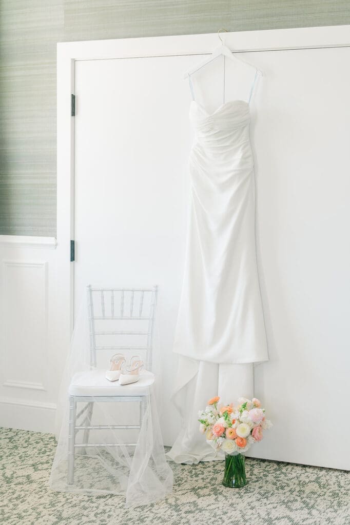 A wedding dress hangs next to her shoes, veil, and bouquet at Wampanoag Country Club. 