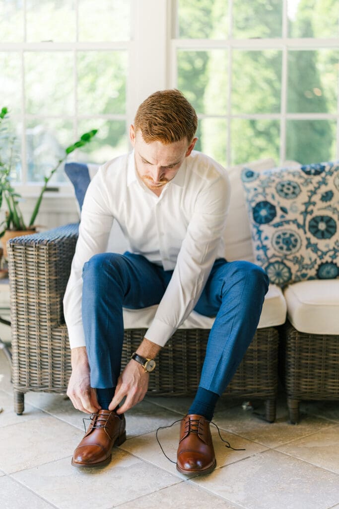 Conor leans over and ties his shoes on his porch. 