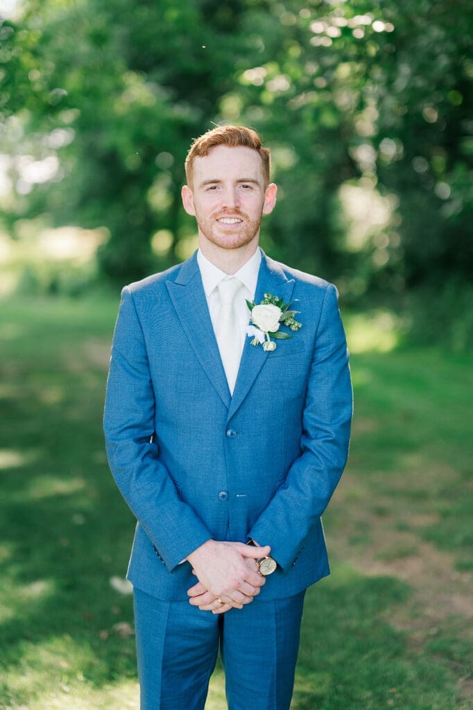 Conor smiles for a classic groom portrait. He is wearing a blue suit. 