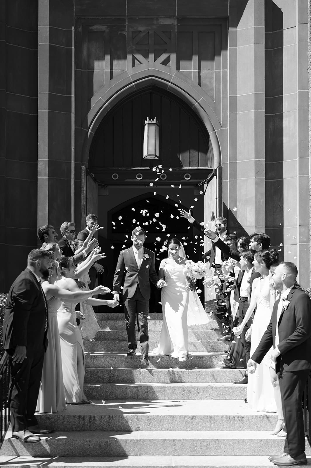 A bride and groom walking out of a church while rose petals are being thrown in the air