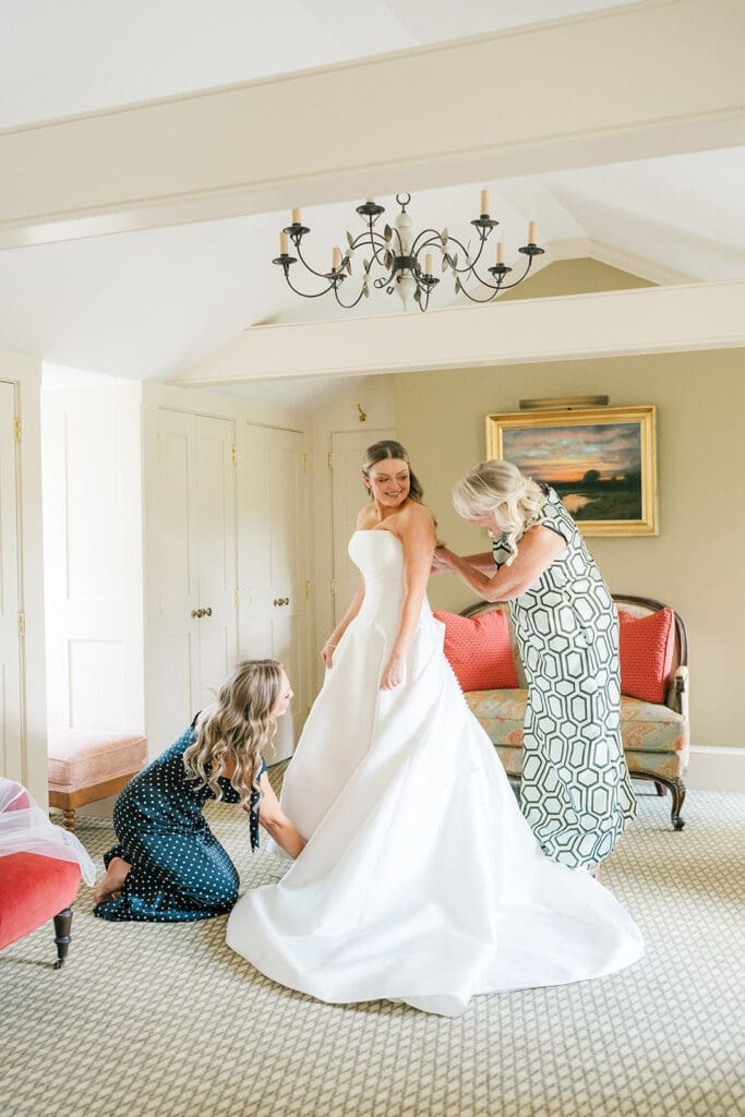 Georgia smiles as her mom and sister help her put on her wedding dress.