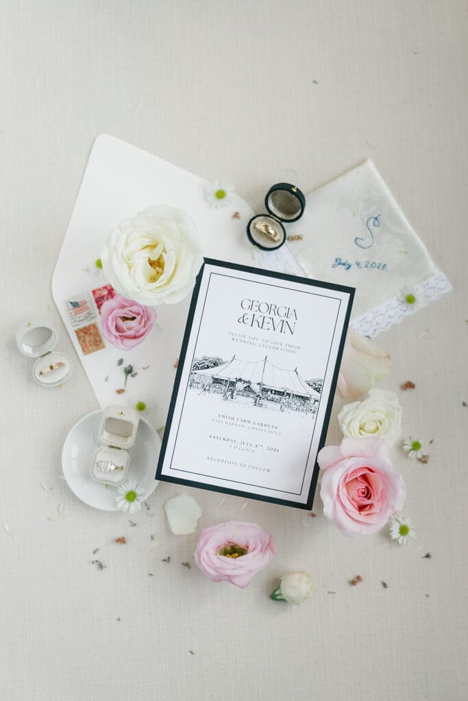 A flat lay with Georgia and Kevin's wedding invitation with pink and white florals around it.