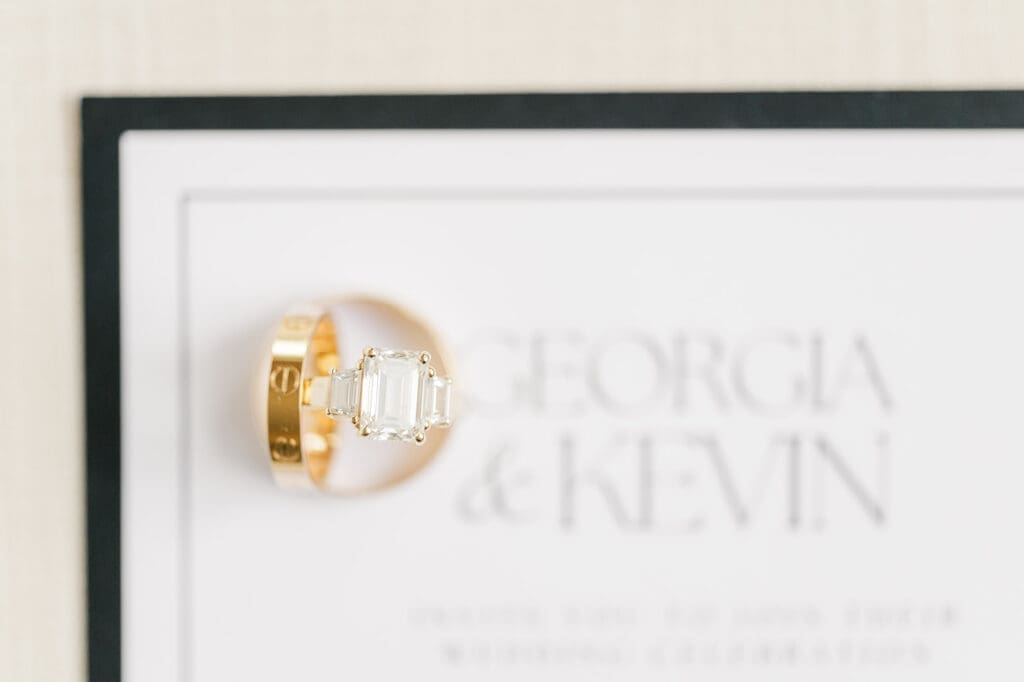 Three wedding bands on top of a wedding invitation that says Georgia and Kevin.
