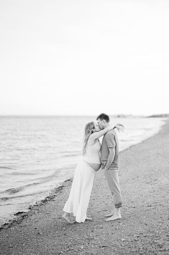 Lindsey leans over and kisses Rich on the water in Westport, CT for their maternity photoshoot in CT.