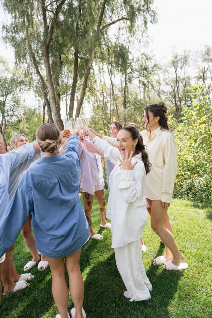 A bride cheers with her bridesmaids and holds up her wedding ring finger. 