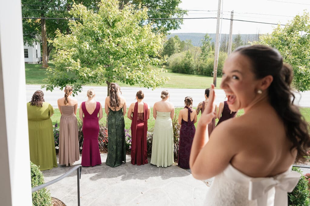A bride does a dress reveal with her bridesmaids outside of the Barnstead Inn. 