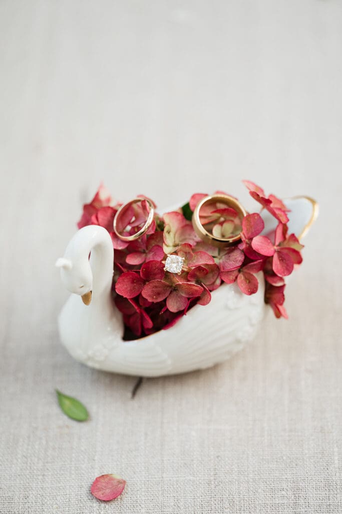A porcelain swan with hydrangeas and wedding rings on it. 