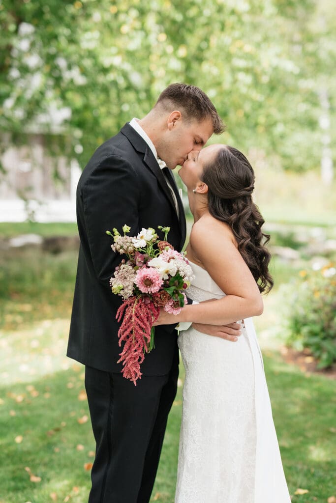 A bride and groom kiss under trees at their wedding at the Barnstead Inn in Vermont. 