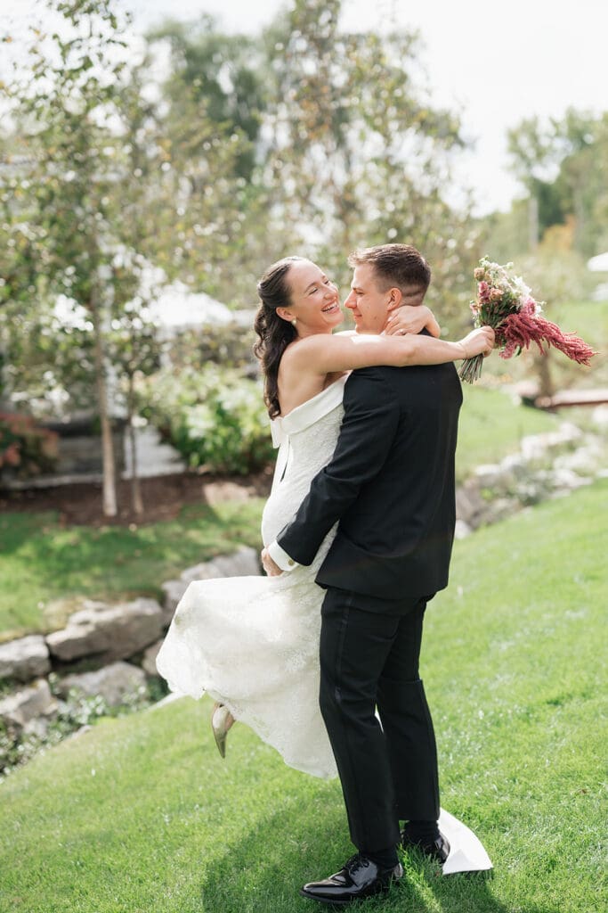 A groom picks up his bride and spins her as they laugh together at their Barnstead Inn wedding. 