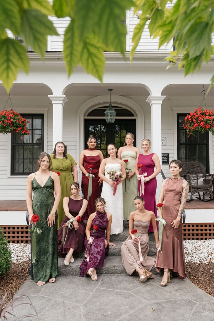 A group of 9 bridesmaids pose on the front steps of the Barnstead Inn for their wedding. 