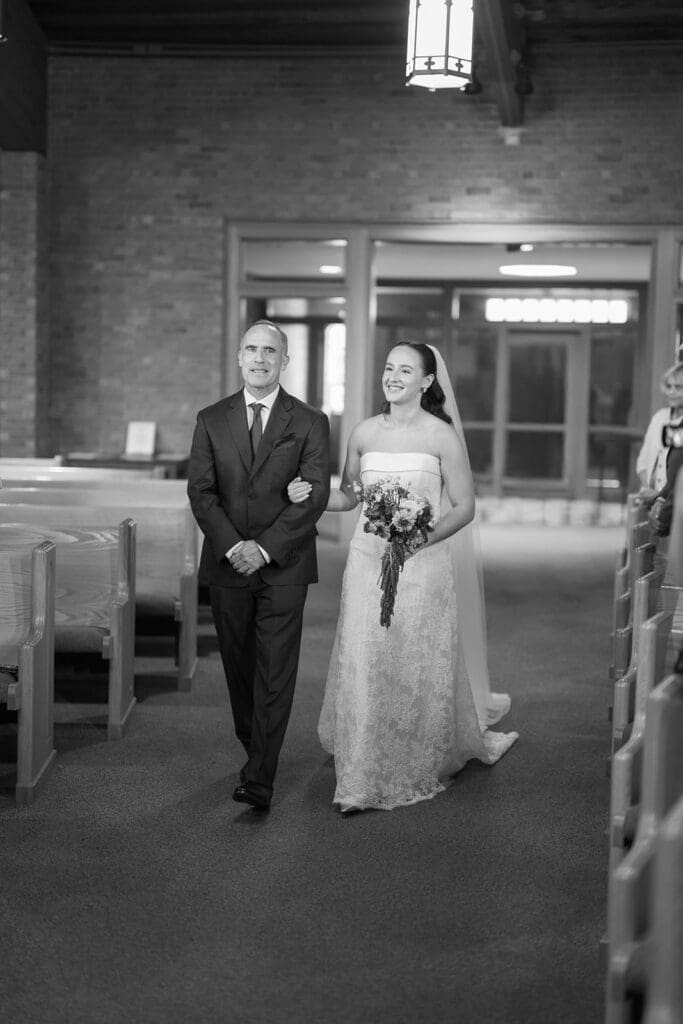 A bride walks down the aisle during her wedding ceremony with her dad. 