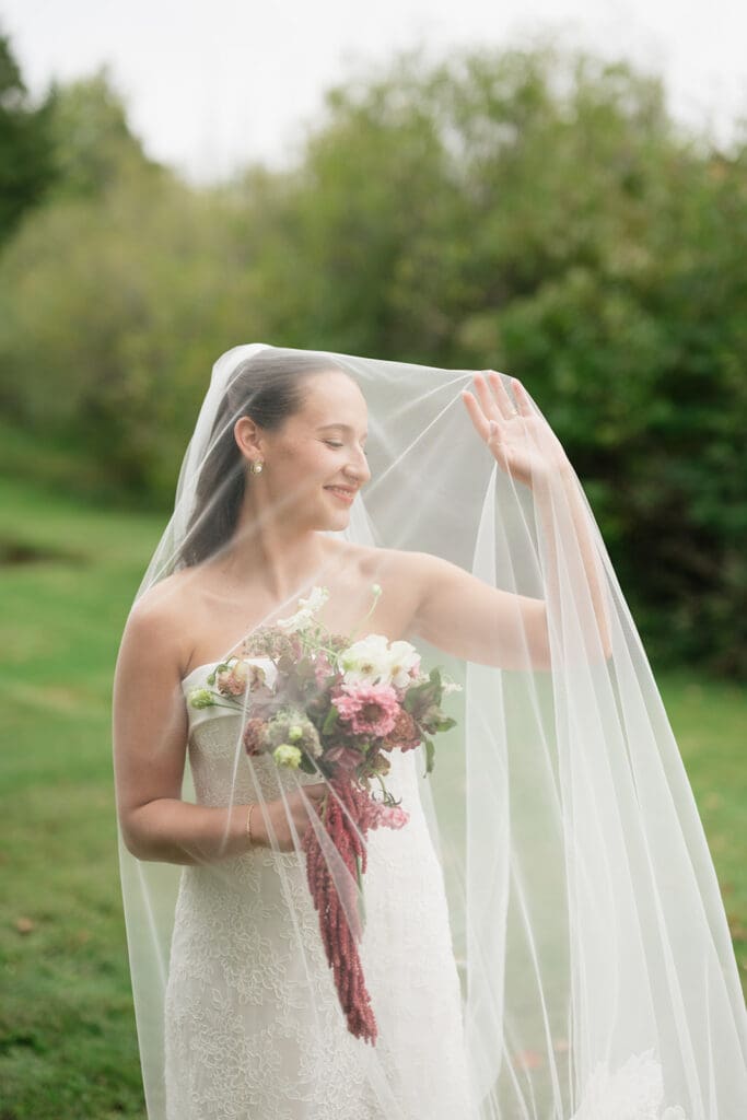 A bride smiles with her veil over her face and plays with it. 