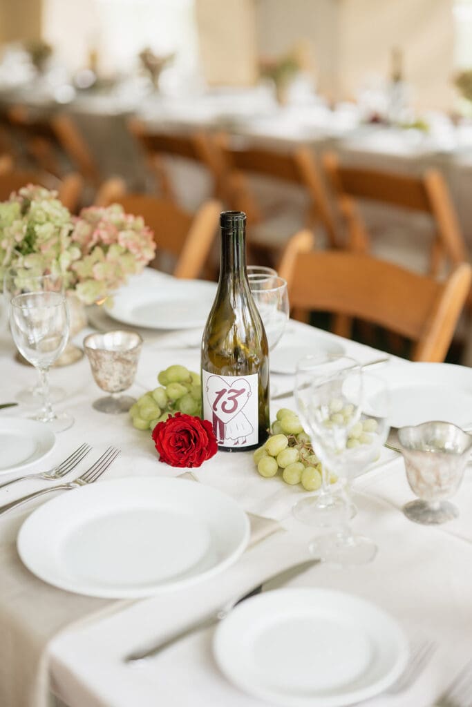A wedding reception tablescape set up. A wine bottle says "13" on it. 