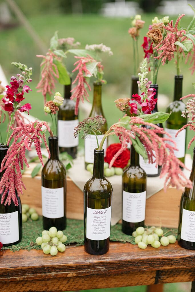 Empty wine bottles filled with purple and green florals as a seating chart at a wedding. 