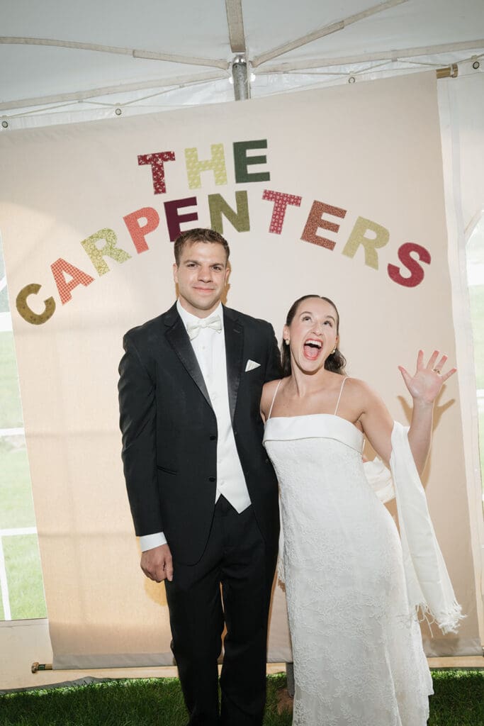 A bride and groom smile under a sign that says "THE CARPENTERS"