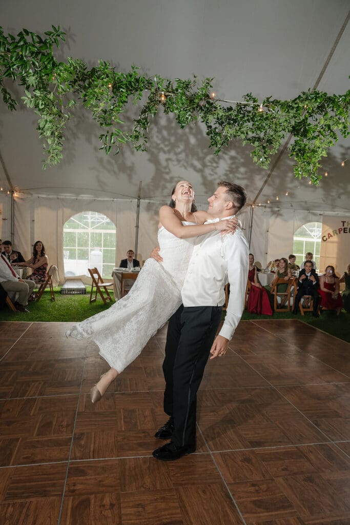The groom carries the bride as they dance during their first dance. 