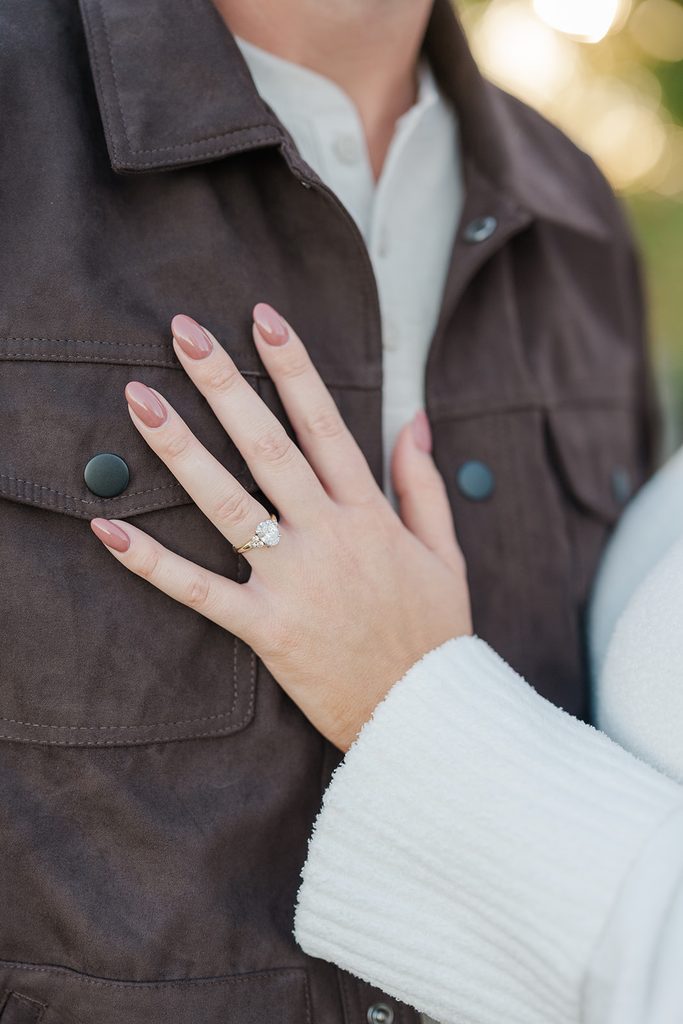 Close-up of an engagement ring on a hand resting on a brown jacket during a fall engagement session in Connecticut