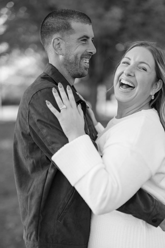 Black and white close-up of an engaged couple laughing together, her ring hand on his chest, during their Connecticut engagement session